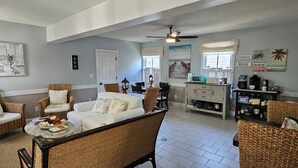 A spacious living room with wicker furniture, a dining area, and a kitchen with a coffee station. - Barclay Cottage (Virginia Beach)