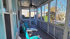 A covered porch with wooden flooring, a ceiling fan, and a row of blue and yellow lounge chairs. - Barclay Cottage (Virginia Beach)