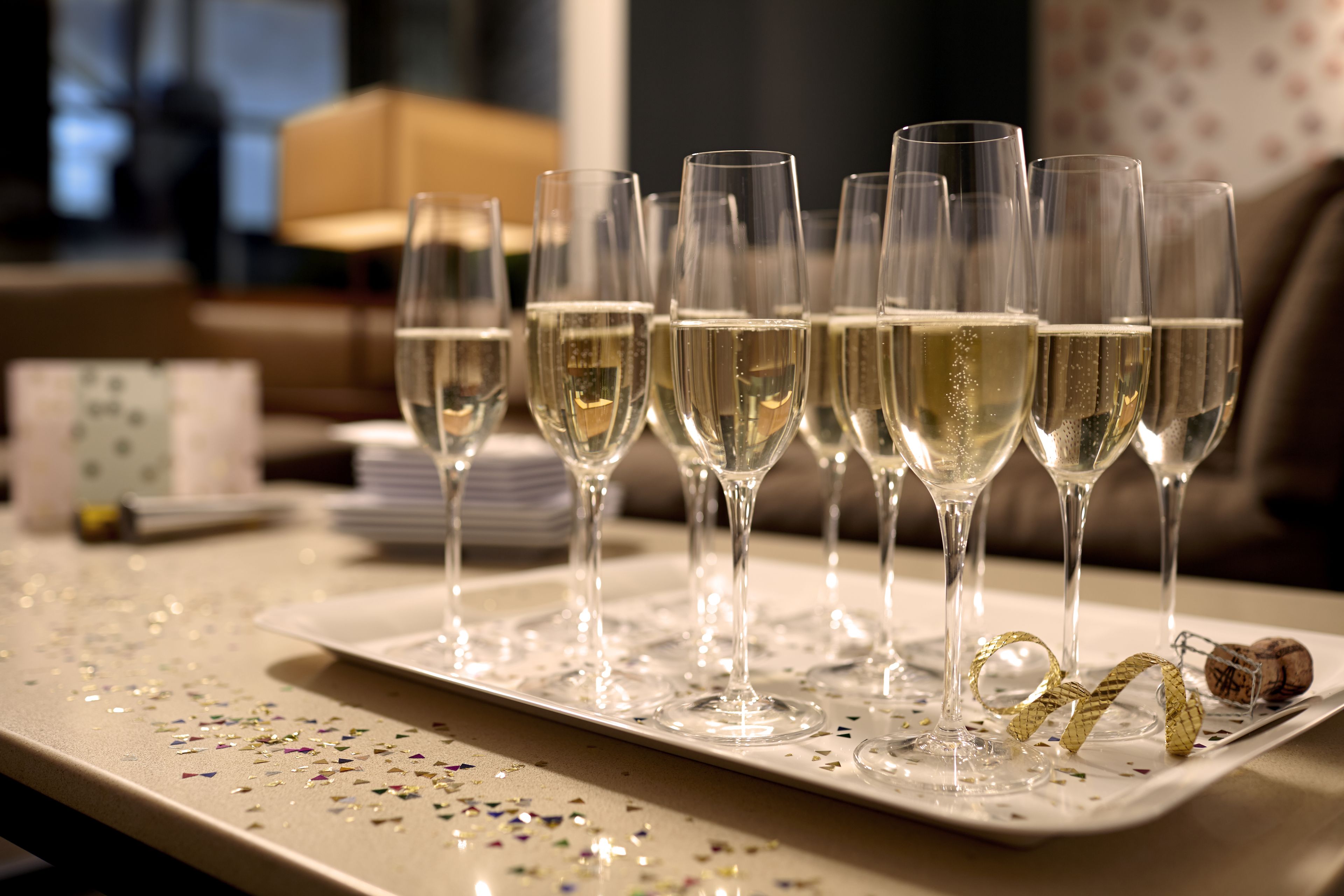 A tray of champagne flutes on a table with confetti, a corkscrew, and a cork.