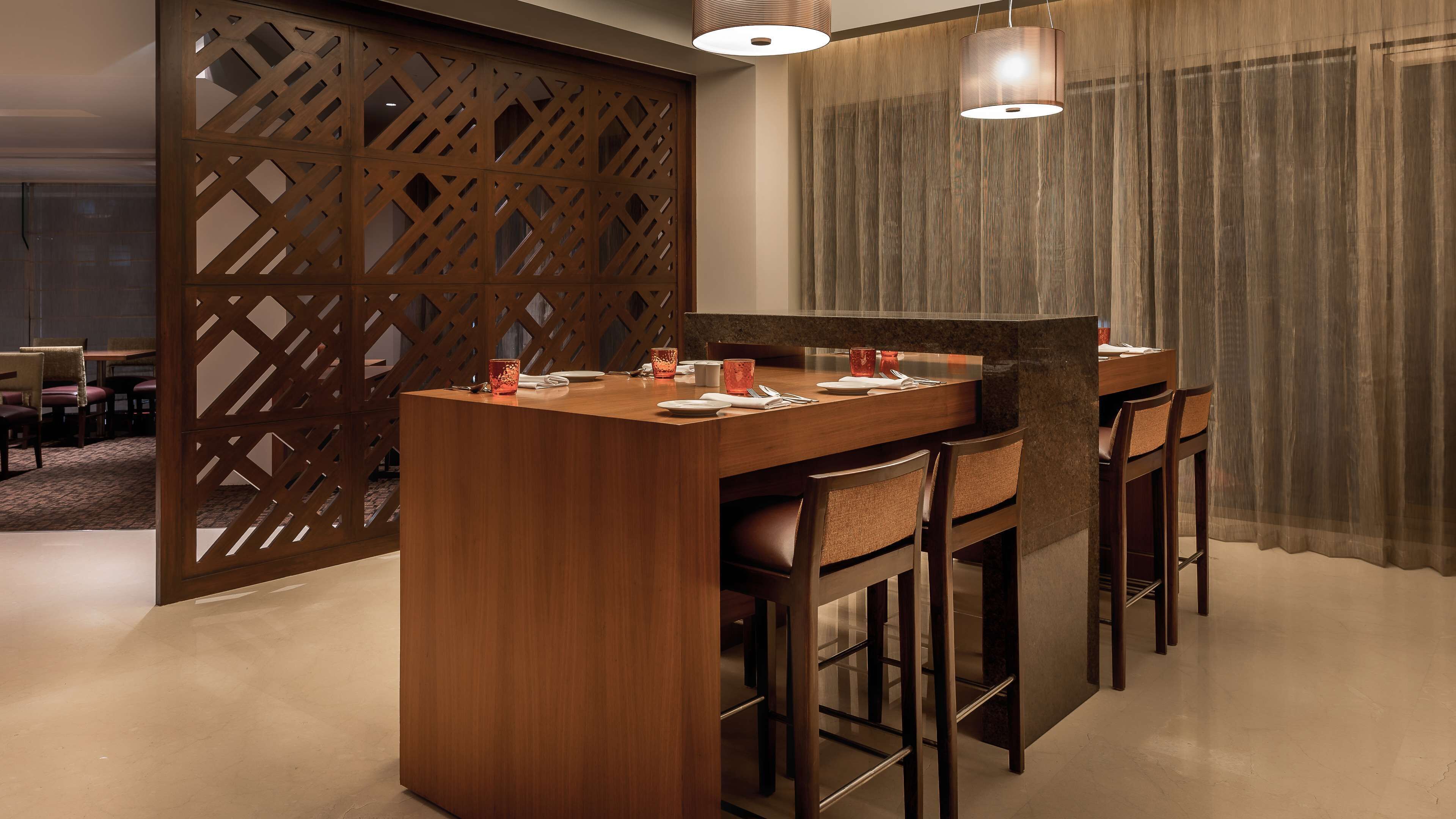 A modern dining area with a wooden bar and bar stools, a partition with a lattice design, and a hanging pendant light.