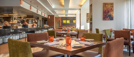 A modern dining area with a central table set for four, surrounded by leather chairs.