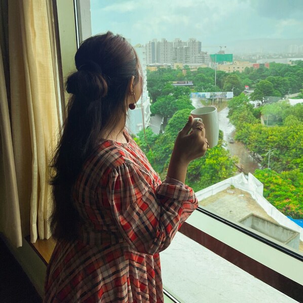 A person holding a mug by a window with a view of a cityscape and greenery. - Hyatt Place Pune/Hinjawadi (Paud)