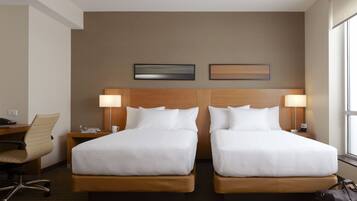 A hotel room with two beds, a desk, a chair, and a window.