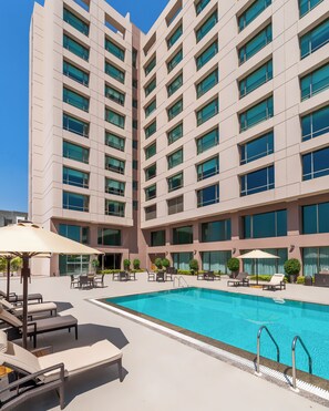 A modern hotel with a swimming pool, outdoor seating, and a large building facade. - Hyatt Place Pune/Hinjawadi (Paud)
