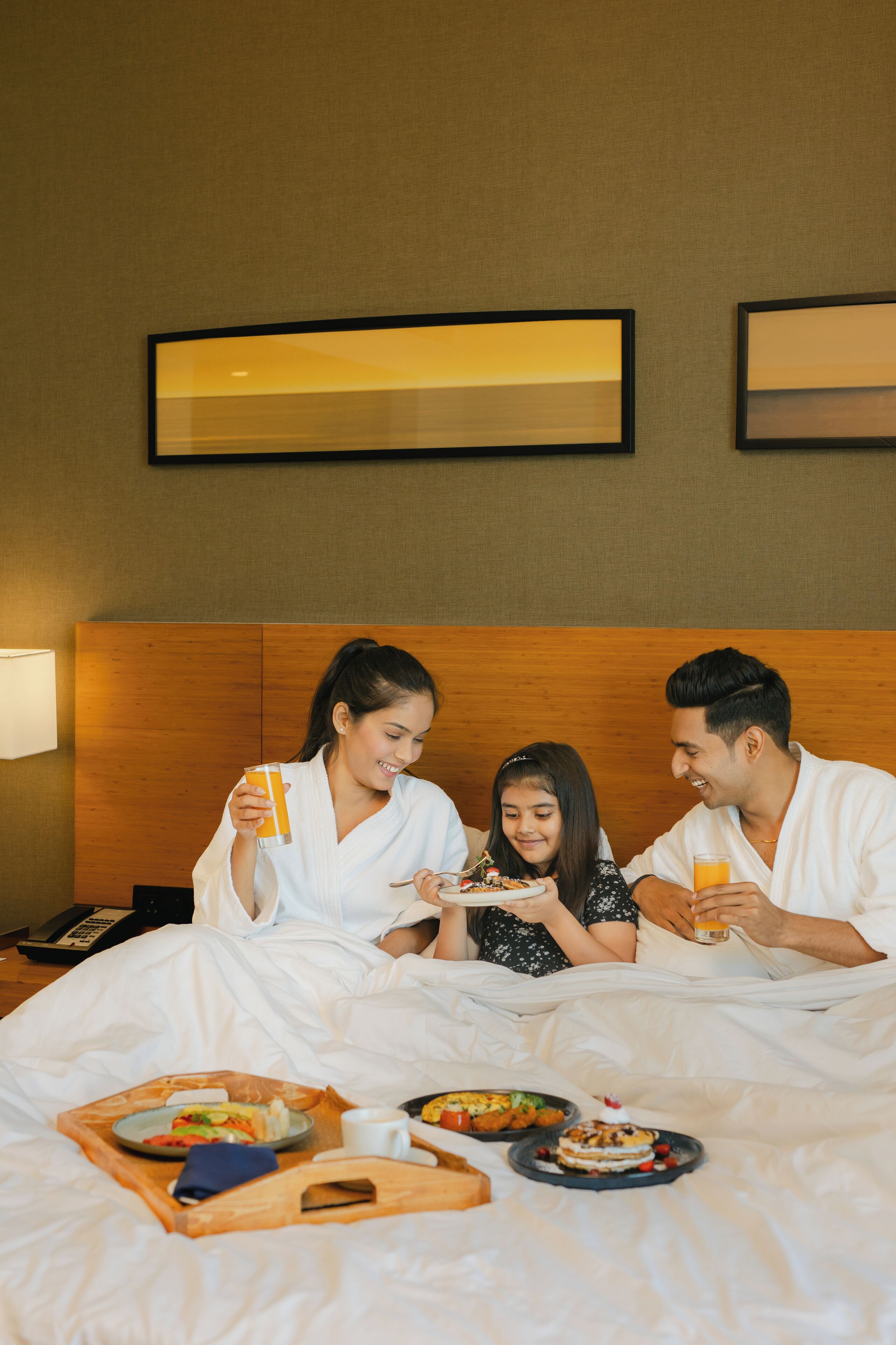 A hotel room with a wooden headboard, a bedside table with a lamp, and a tray with breakfast items.