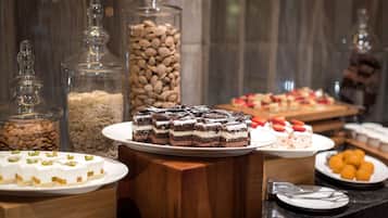 Un bufé con diversos postres, incluyendo pasteles y productos de repostería, dispuesto sobre una mesa de madera con recipientes de vidrio que exhiben frutos secos y otros alimentos al fondo.