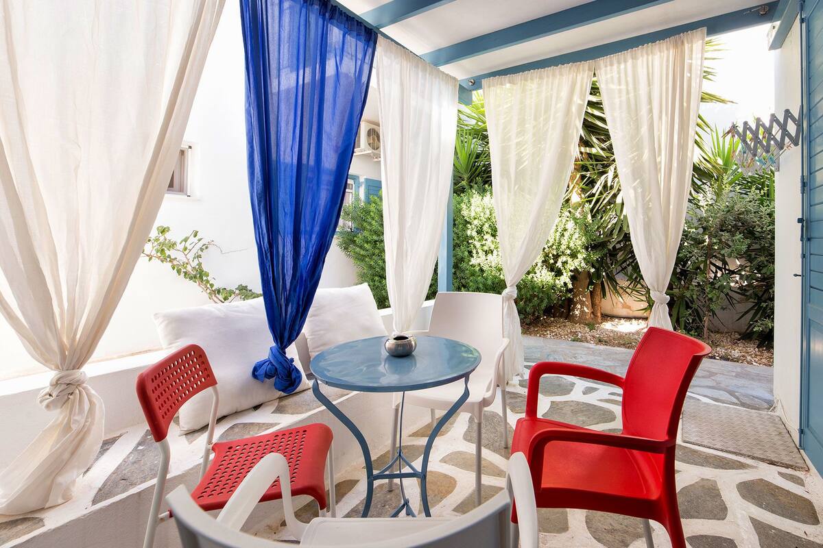 Un patio al aire libre con una mesa redonda y sillas, cubierto por cortinas blancas y azules translúcidas.