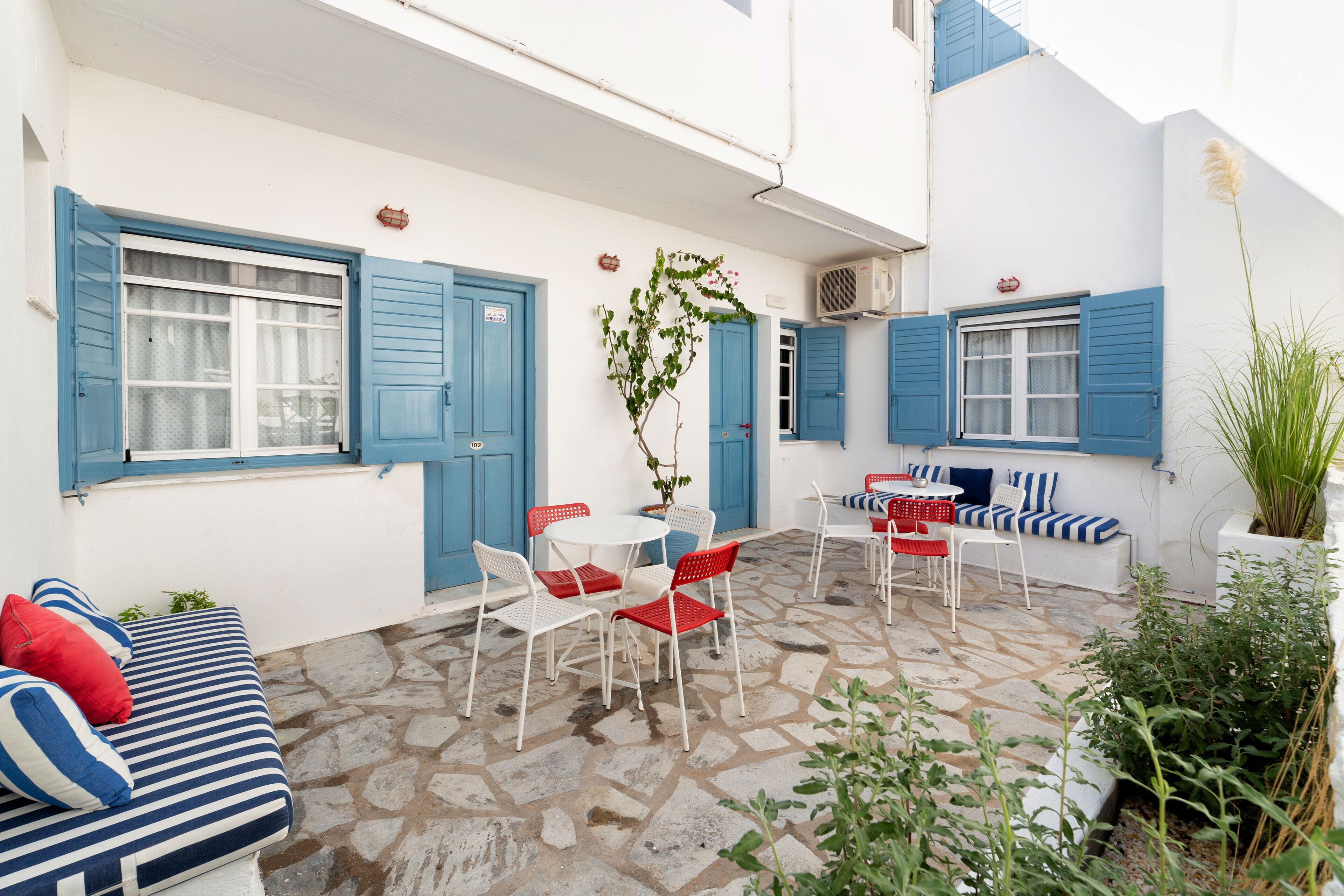 Un patio con suelo de piedra, paredes blancas, contraventanas azules y una zona de estar con mesa y sillas.