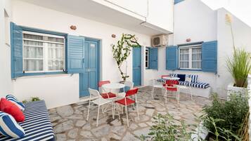 Un patio con suelo de piedra, paredes blancas, contraventanas azules y una zona de estar con mesa y sillas.