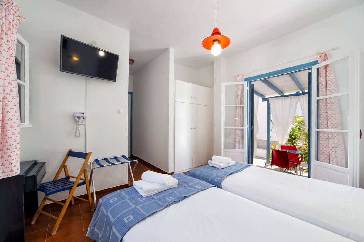 Un dormitorio con dos camas, televisión, una silla y una mesa cerca de una ventana.