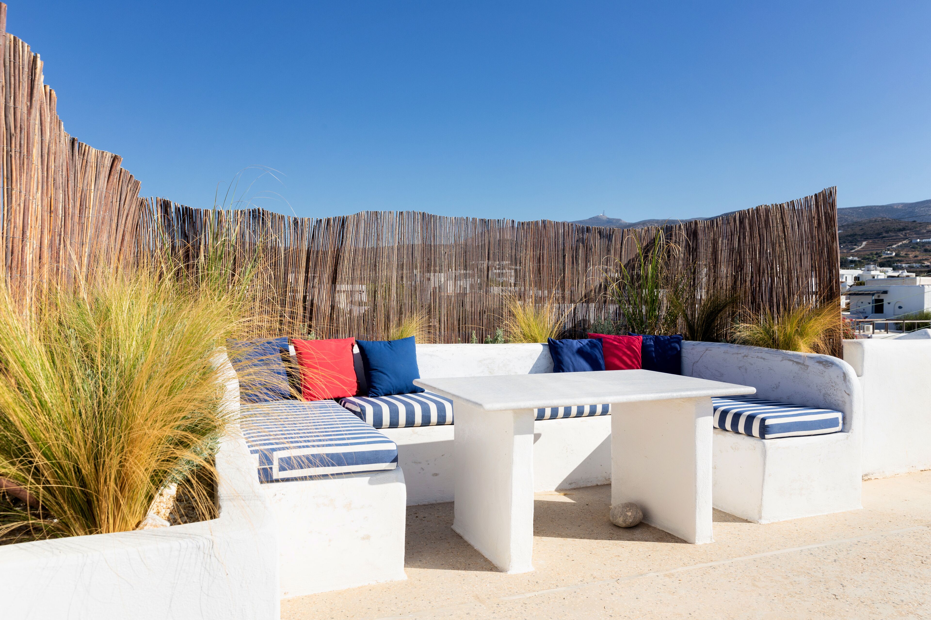A rooftop terrace with white outdoor furniture, including a sofa and a table, and a wooden fence in the background.