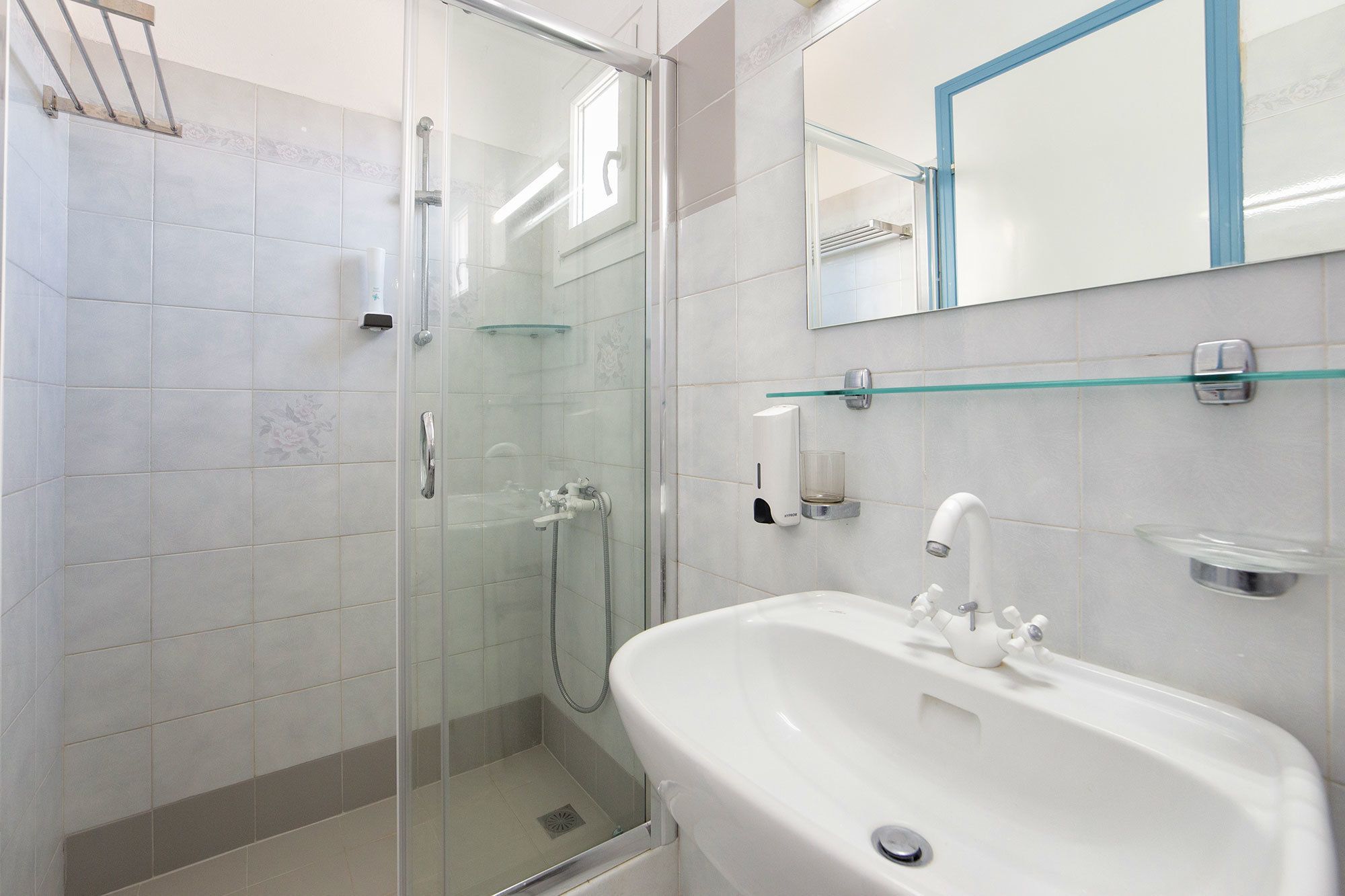 A modern bathroom with a glass-enclosed shower, a white sink with a single faucet, and a mirror above the sink.