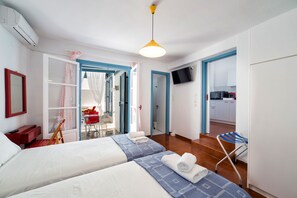 A hotel room with two beds, a TV, a kitchenette, and a bathroom visible through an open door. - Fivos Apartments (Paros)