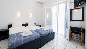 A modern hotel room with two beds, a small desk, a mirror, and a television. - Fivos Apartments (Paros)