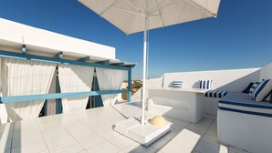 A rooftop terrace with a white table, blue-framed window, and a white umbrella. - Fivos Apartments (Paros)