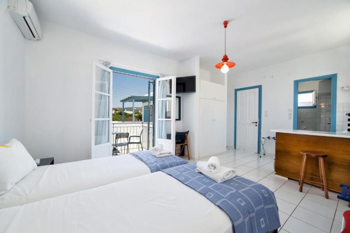 A hotel room with two beds, a balcony, a kitchen area, and a TV.