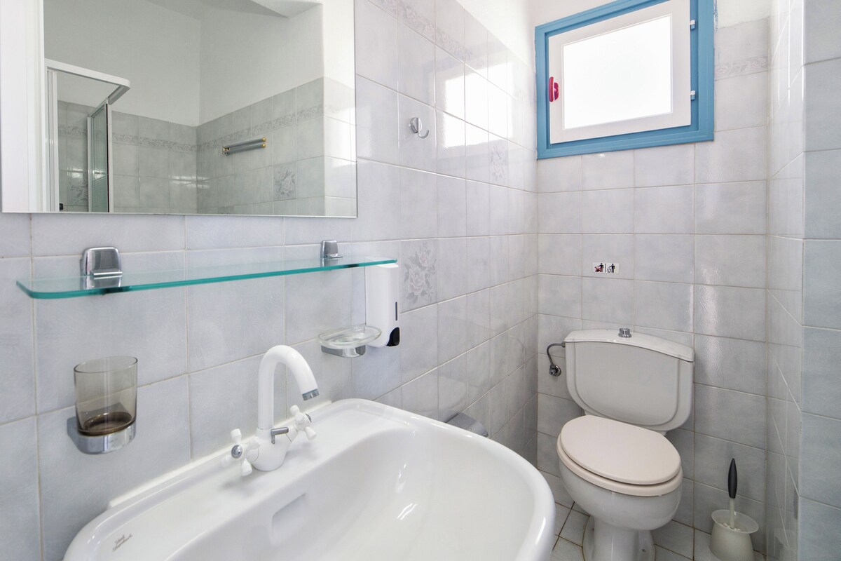 A modern bathroom with a white sink, glass shelf, and a toilet.