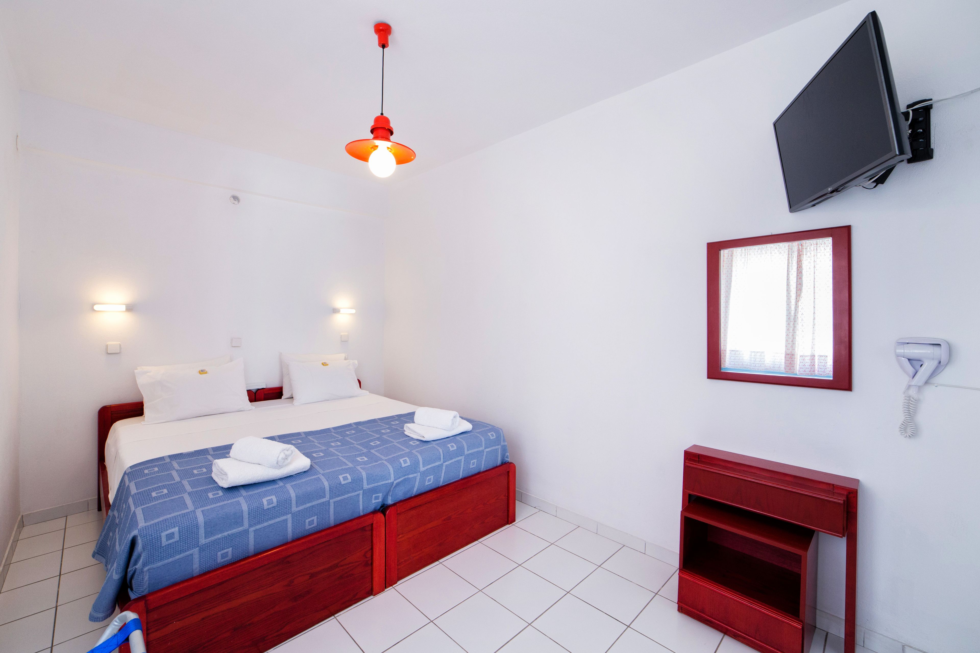 A hotel room with a bed, a TV mounted on the wall, a window, and a telephone.