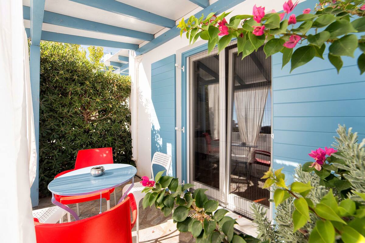 Un patio con fachada azul y blanca, una puerta corrediza de vidrio y una pequeña mesa con sillas.