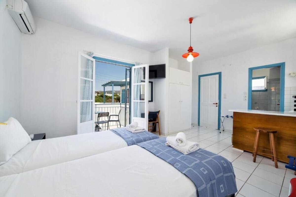 Habitación de hotel con dos camas, balcón, zona de cocina y televisor.