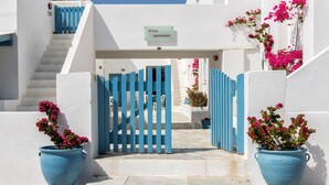 A white building with a blue gate and steps leading to an entrance. - Fivos Apartments (Paros)