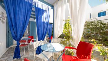 Une terrasse agrémentée de rideaux bleus et blancs, de chaises rouges et blanches, et d’une table en verre.