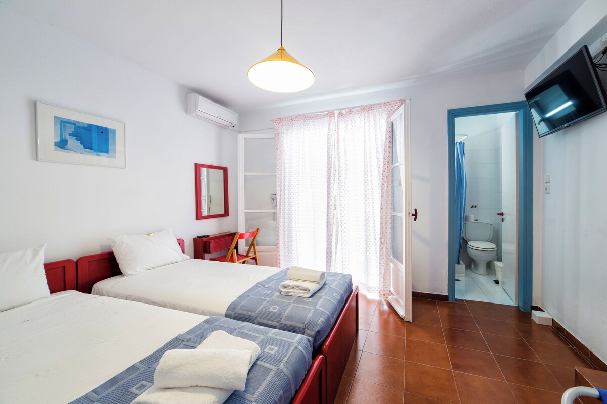 A hotel room with two beds, a red chair, a TV, and a bathroom visible through an open door.