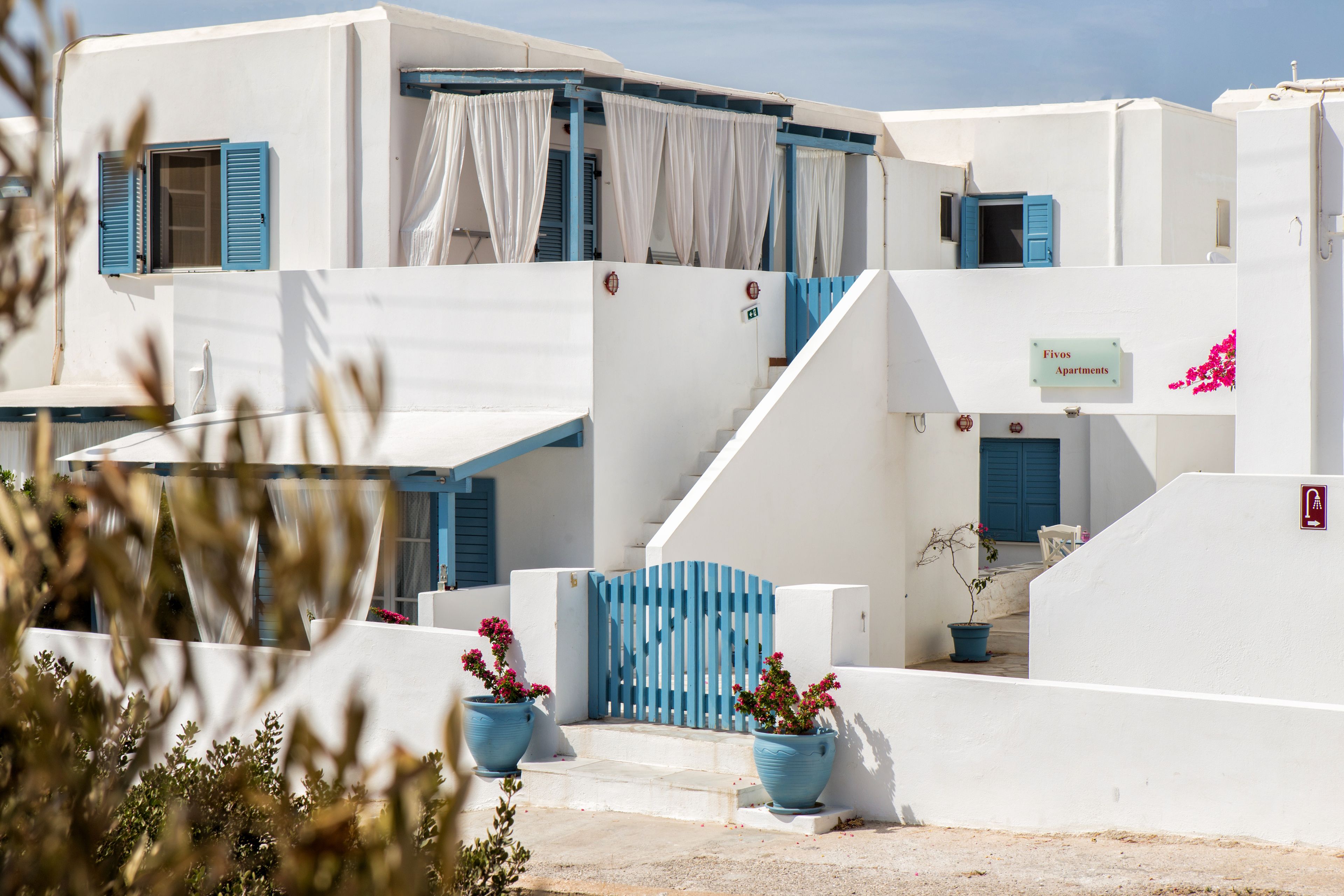 Un edificio blanco con contraventanas azules y un letrero que dice 'Fivos Apartments'.
