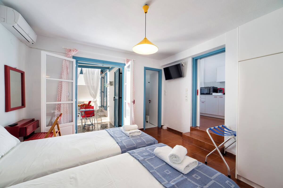 Habitación de hotel con dos camas, un televisor, una silla roja y vista a la cocina.