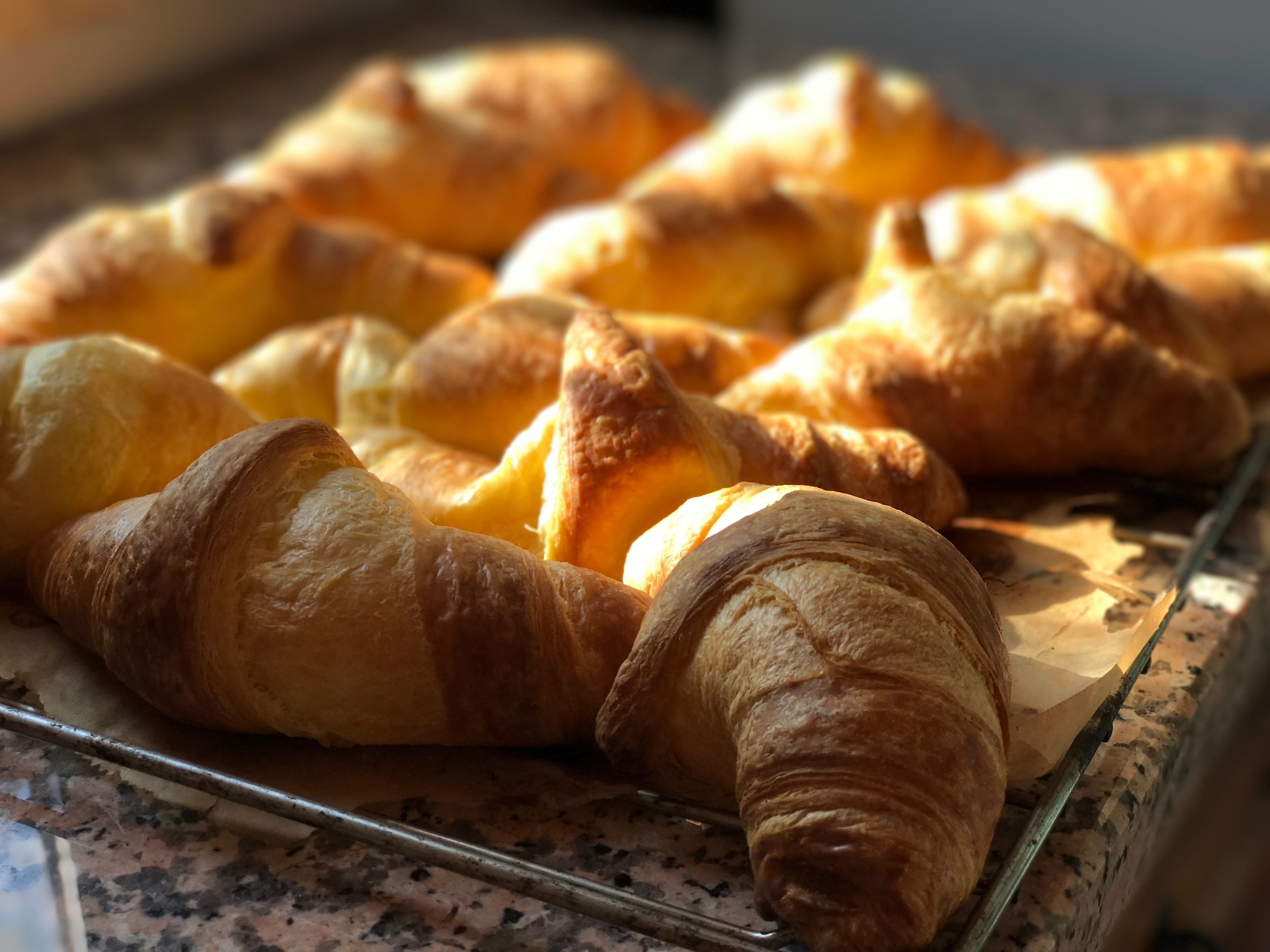 A tray of golden-brown croissants on a marble countertop.