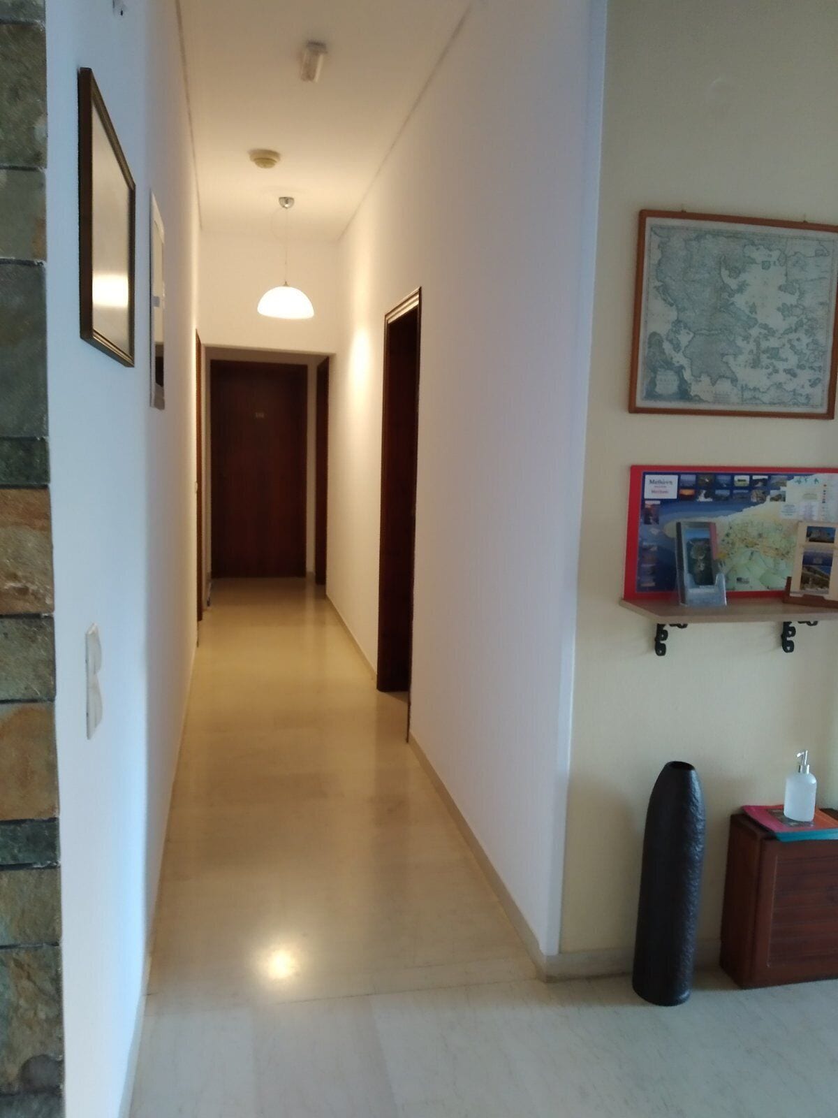 A hallway with a wooden door at the end, a wall-mounted map, and a small cabinet with a bottle.