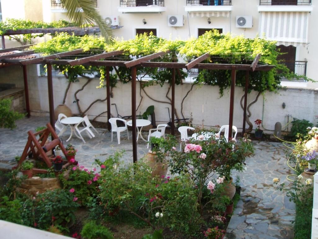 An outdoor patio with a pergola, white plastic chairs, and a stone pathway.