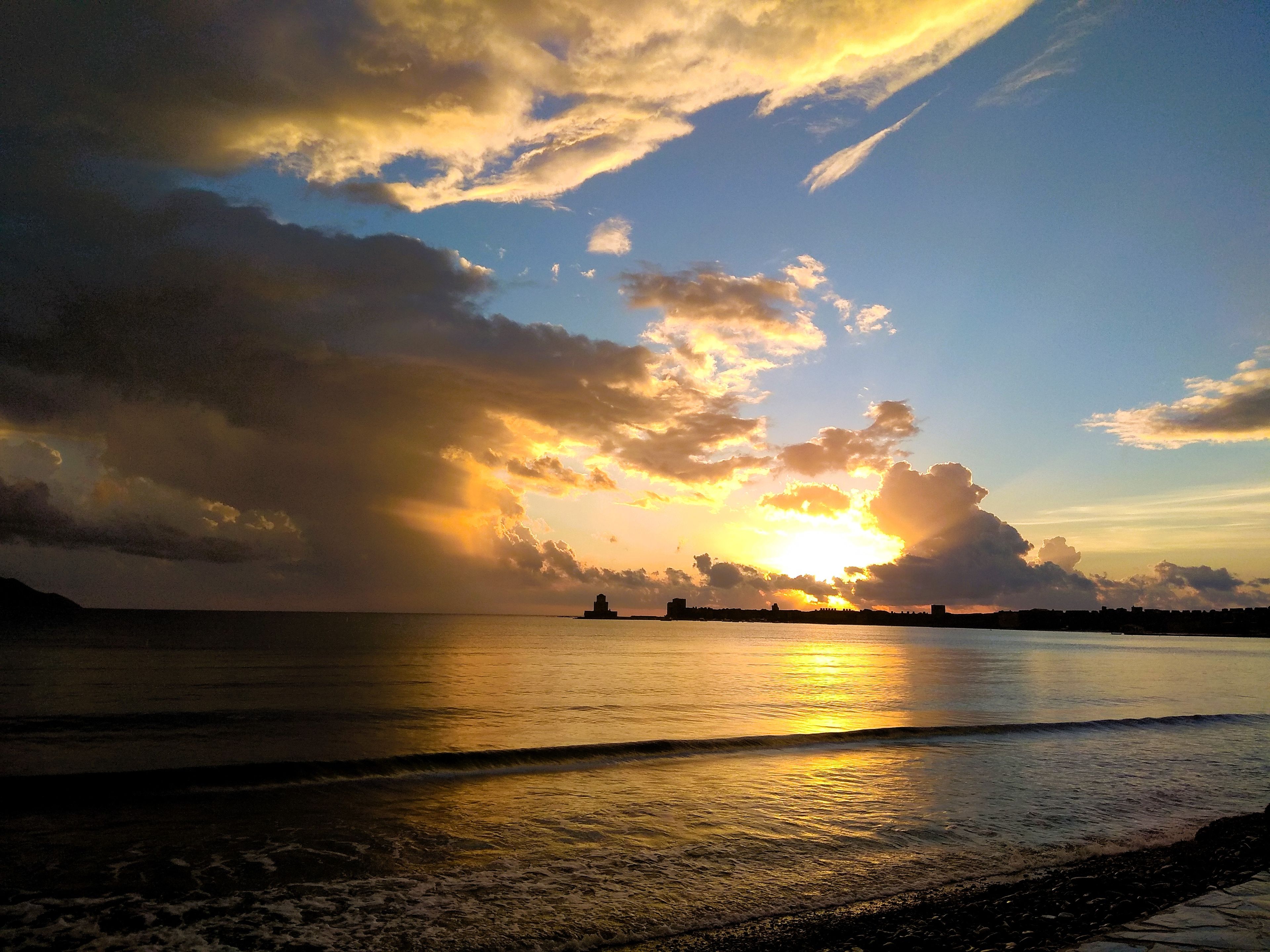 A sunset over a calm sea with a distant shoreline.