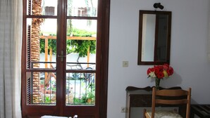 Una habitación con puerta de madera, un espejo, una silla y un florero con flores.