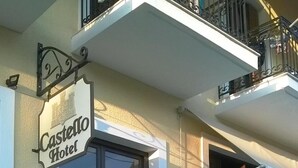 Exterior del Hotel Castello, con una fachada moderna, una entrada destacada con puerta de vidrio y un balcón con barandas de metal.