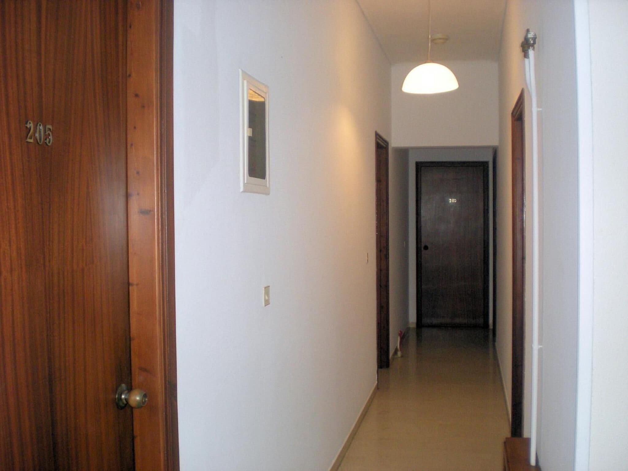 A narrow hallway with a wooden door labeled "205" on the left, a small window, and a door at the end.