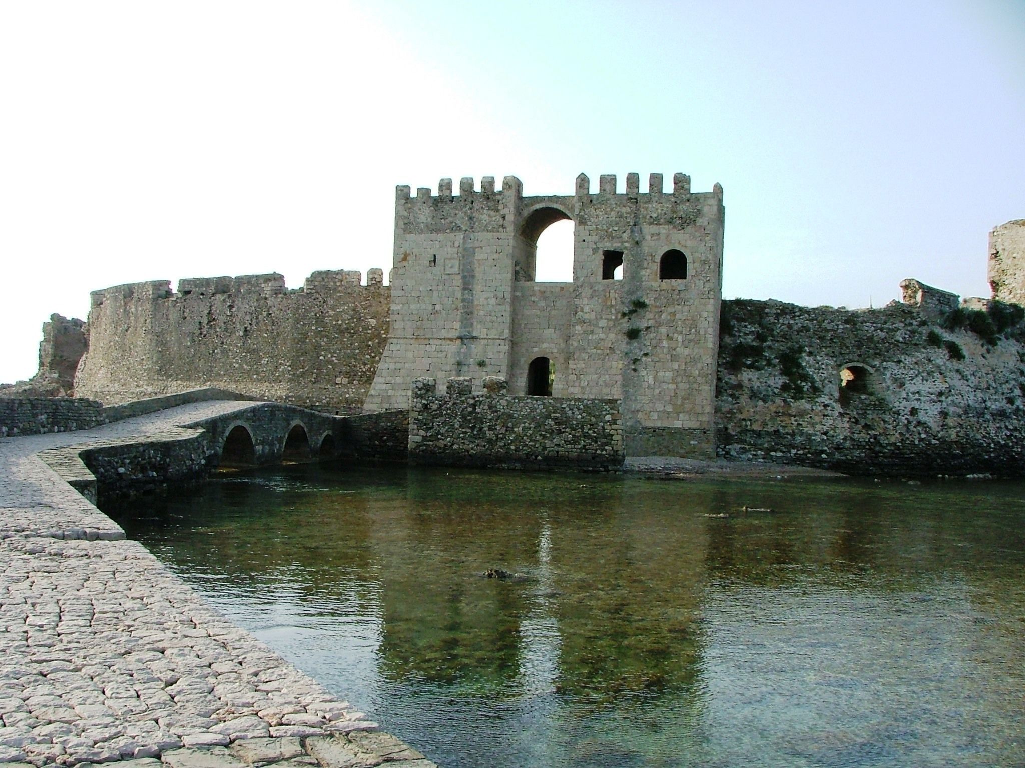 A historic stone bridge leading to a fortified castle with a moat.