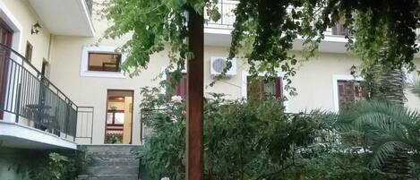 Un edificio con una escalera que lleva a una puerta, rodeado de abundante vegetación y una palmera.