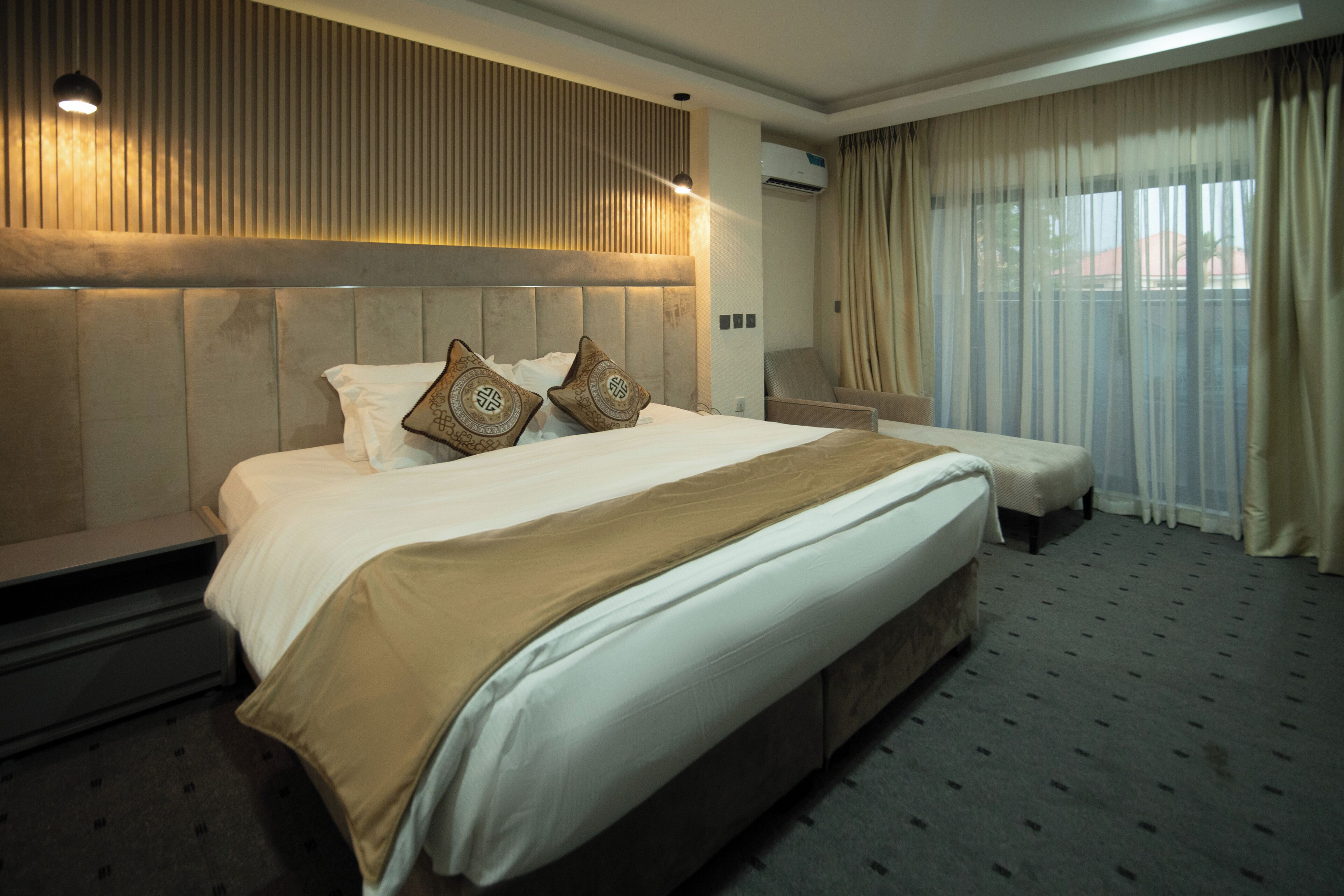 Ein Hotelzimmer mit einem großen Bett, einem Nachttisch, einem Sessel und einem Fenster mit Vorhängen.