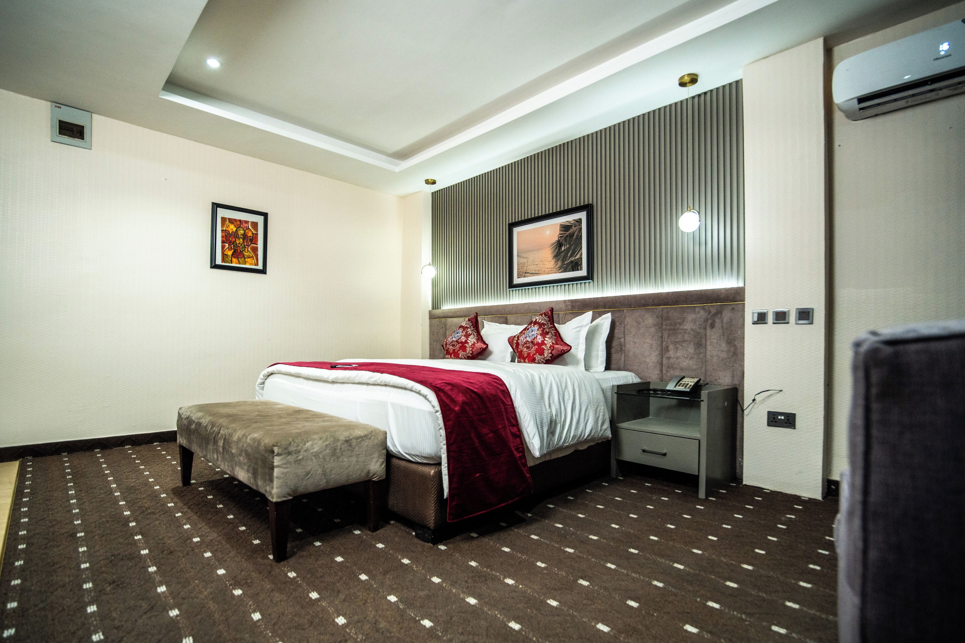 A modern hotel room with a large bed, a bedside table, a nightstand, and a small seating area.