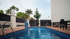 A swimming pool with a tiled edge, surrounded by a patio area with chairs and a fence. - Vynedresa Hotel (Abuja)