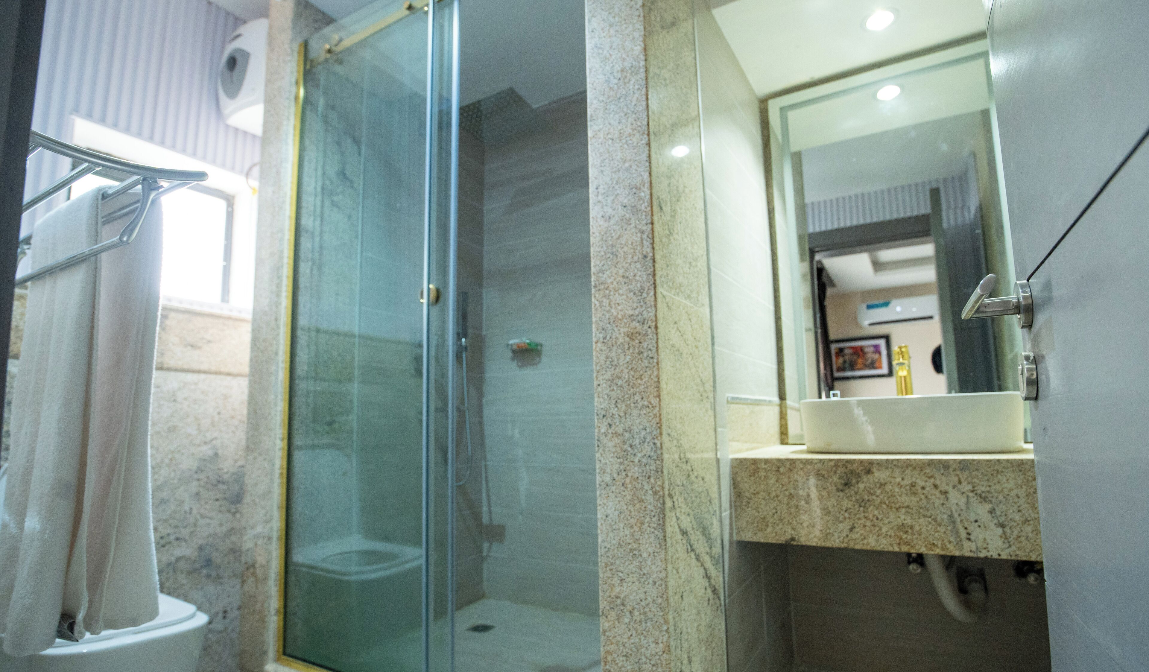 A modern bathroom with a glass shower enclosure, a toilet, and a sink with a marble countertop.
