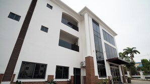 A multi-story building with a white facade, large windows, and a brick base. - Vynedresa Hotel (Abuja)