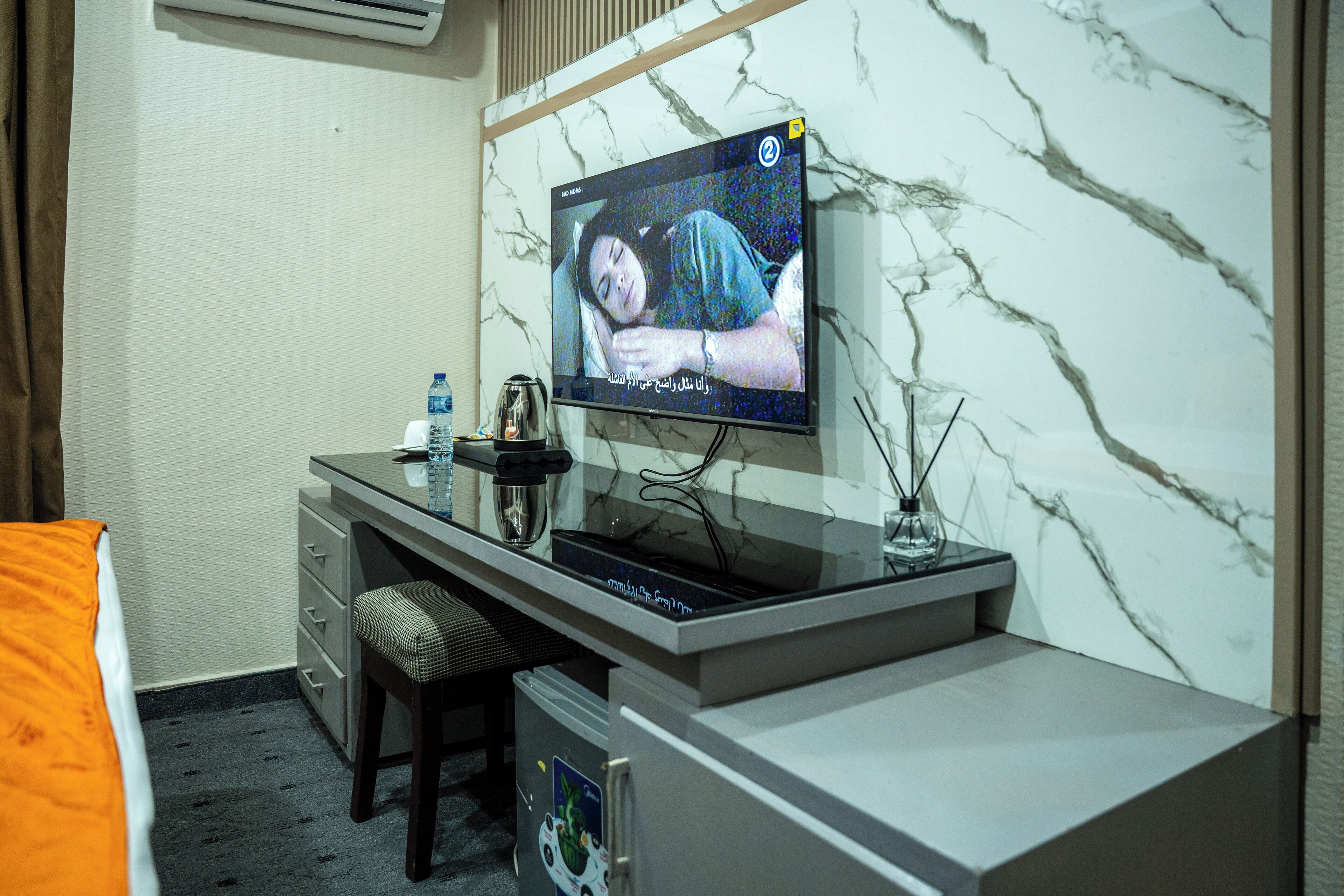 A hotel room with a bed, a desk with a computer, a television, and a marble wall.