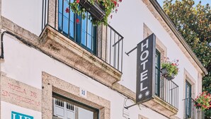 La façade d’un hôtel, avec une porte verte, une enseigne indiquant le service des ressources humaines, et un balcon orné de plantes en suspension.