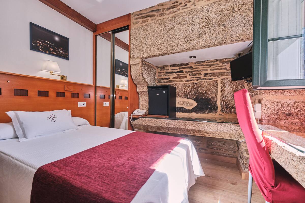 Une chambre d’hôtel avec un lit, un bureau, un mur en pierre et un tableau représentant une vue nocturne accroché au mur.