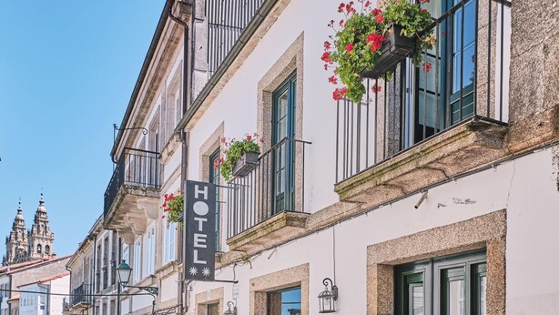 Un hôtel avec une enseigne, une façade en pierre et des balcons ornés de jardinières.