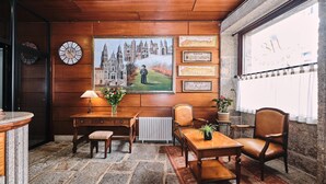 Une pièce avec un plafond en bois, un sol en pierre, un bureau avec une lampe, une chaise, un radiateur et un tableau représentant un château.