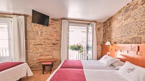 Une chambre d’hôtel avec deux lits, une tête de lit en bois, une petite table, un banc et un mur en pierre.