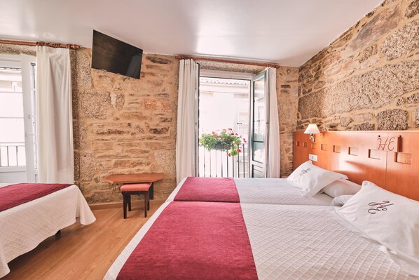 A hotel room with two beds, a wooden headboard, a small table, a bench, and a stone wall. - Hotel Entrecercas (Santiago de Compostela)